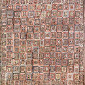 Woven rug displaying a structured grid of geometric square designs colored red, navy, black, and cream.