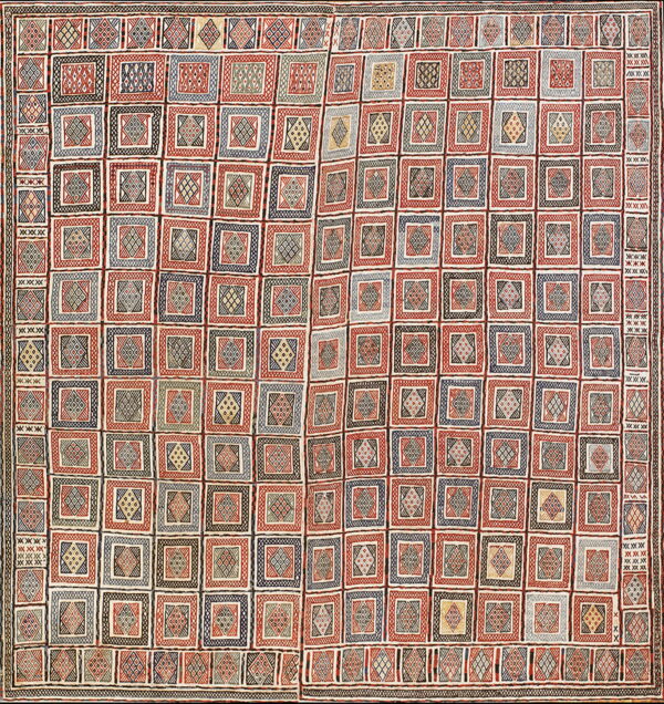 Woven rug displaying a structured grid of geometric square designs colored red, navy, black, and cream.