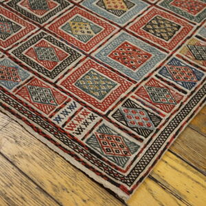 Red, blue, and beige geometric patterned rug with textured diamonds covers a distressed wood floor.