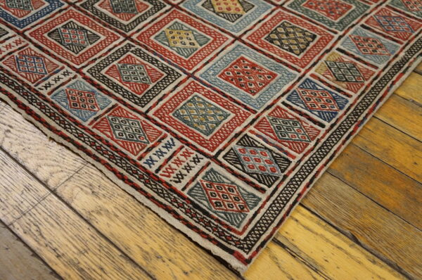 Red, blue, and beige geometric patterned rug with textured diamonds covers a distressed wood floor.