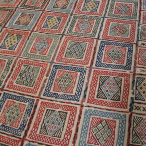 Textural low-pile rug displaying repeating geometric squares and diamond motifs in red, blue, green, and cream.