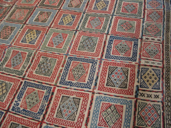 Textural low-pile rug displaying repeating geometric squares and diamond motifs in red, blue, green, and cream.