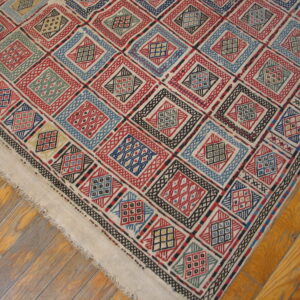 Geometric diamond pattern rug in red, blue, black, and natural cream colors on wood flooring.