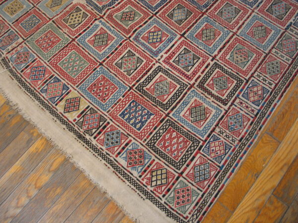 Geometric diamond pattern rug in red, blue, black, and natural cream colors on wood flooring.