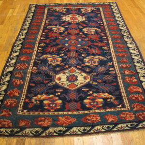 Navy blue, red, and teal geometric rug with a central medallion and complex borders on hardwood.