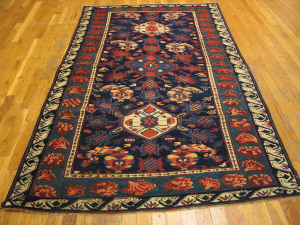 Navy blue, red, and teal geometric rug with a central medallion and complex borders on hardwood.
