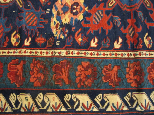 Close-up of a rug featuring geometric and floral borders in navy, red, teal, and cream colors.