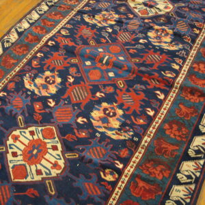 A densely patterned blue and red rug with thick pile rests on light brown wooden floorboards.