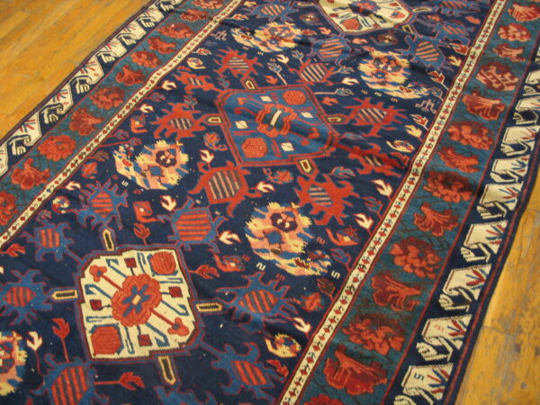 A densely patterned blue and red rug with thick pile rests on light brown wooden floorboards.