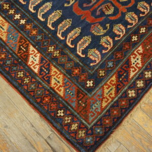 Detailed corner of a low-pile rug with navy, red, and beige geometric patterns on distressed wood planks.