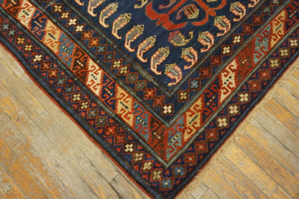Detailed corner of a low-pile rug with navy, red, and beige geometric patterns on distressed wood planks.