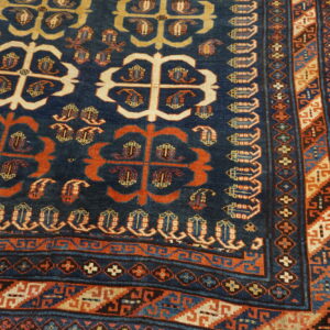 Navy blue rug with stylized orange and cream motifs, detailed geometric borders, resting on light hardwood.