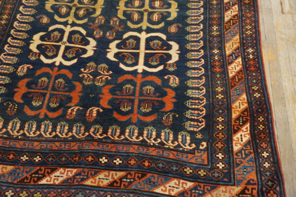 Navy blue rug with stylized orange and cream motifs, detailed geometric borders, resting on light hardwood.