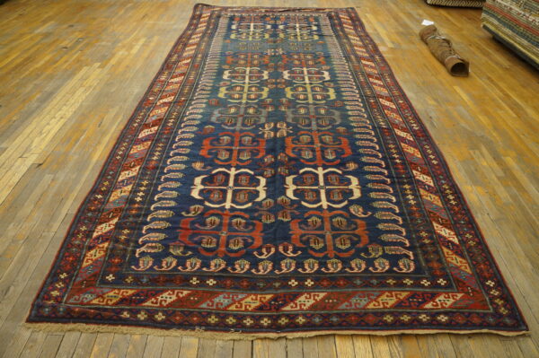 Dark blue runner rug featuring repeating red and beige geometric motifs on a wide plank wood floor.