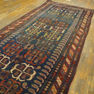 A navy rug with repeating rust and cream geometric medallions is spread out on light wooden floorboards.