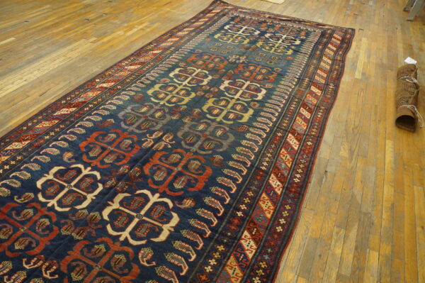 A navy rug with repeating rust and cream geometric medallions is spread out on light wooden floorboards.