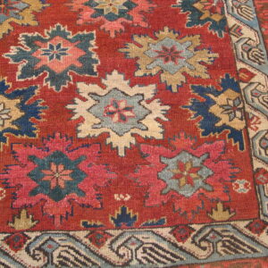 Red rug displaying stylized geometric star motifs in shades of blue, cream, pink, and tan.