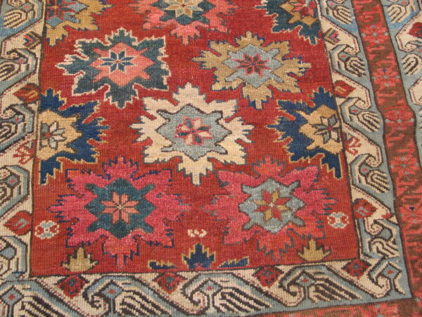Red rug displaying stylized geometric star motifs in shades of blue, cream, pink, and tan.