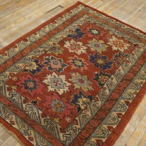 Reddish-orange rug featuring blue, cream, and green geometric motifs with multiple patterned borders on wood planks.