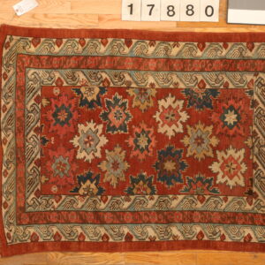 Low-pile area rug with complex red, teal, and cream medallions and borders on hardwood floor.