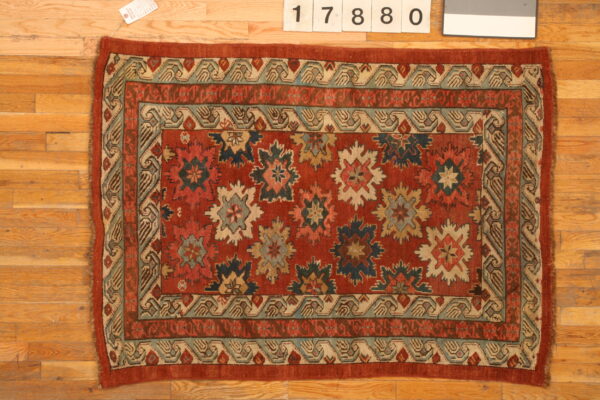 Low-pile area rug with complex red, teal, and cream medallions and borders on hardwood floor.