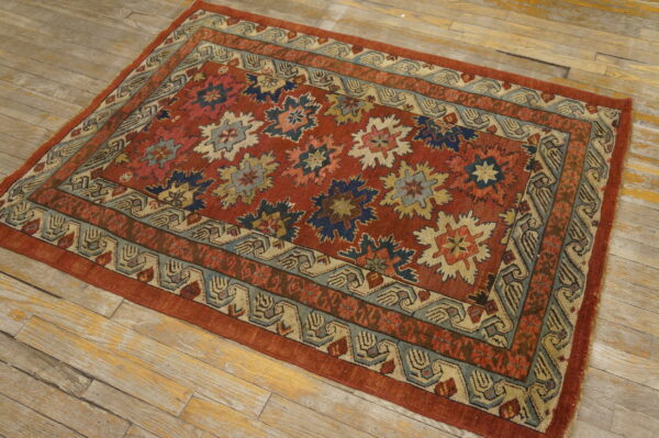 Rust-red geometric rug with blue and tan patterns on distressed light wooden floorboards.
