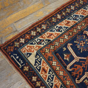 Low-pile rug corner with geometric patterns in navy, rust, and cream on distressed wood floorboards.