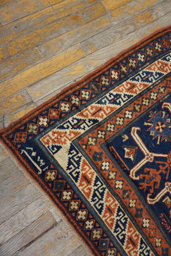 Low-pile rug corner with geometric patterns in navy, rust, and cream on distressed wood floorboards.