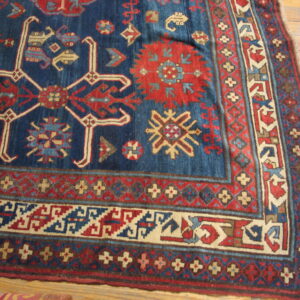 Detailed corner of a blue and red geometric rug with multiple borders resting on wood plank flooring.