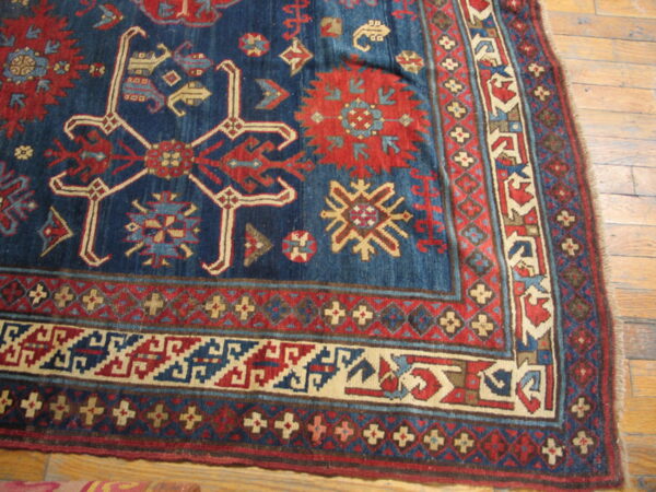 Detailed corner of a blue and red geometric rug with multiple borders resting on wood plank flooring.