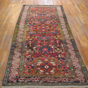 Runner rug in red, brown, blue, and green colors, featuring stylized geometric patterns on a wood plank floor.