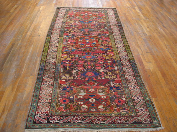 Runner rug in red, brown, blue, and green colors, featuring stylized geometric patterns on a wood plank floor.