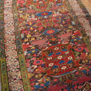 Angled view of a detailed runner rug featuring red, blue, green, and black patterns on wood planks.