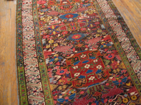 Angled view of a detailed runner rug featuring red, blue, green, and black patterns on wood planks.