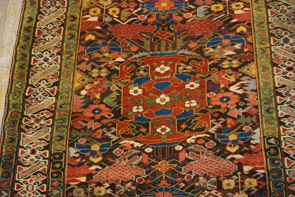Intricate traditional rug with a dark field, red central design, multi-colored motifs, and green borders on wood planks.