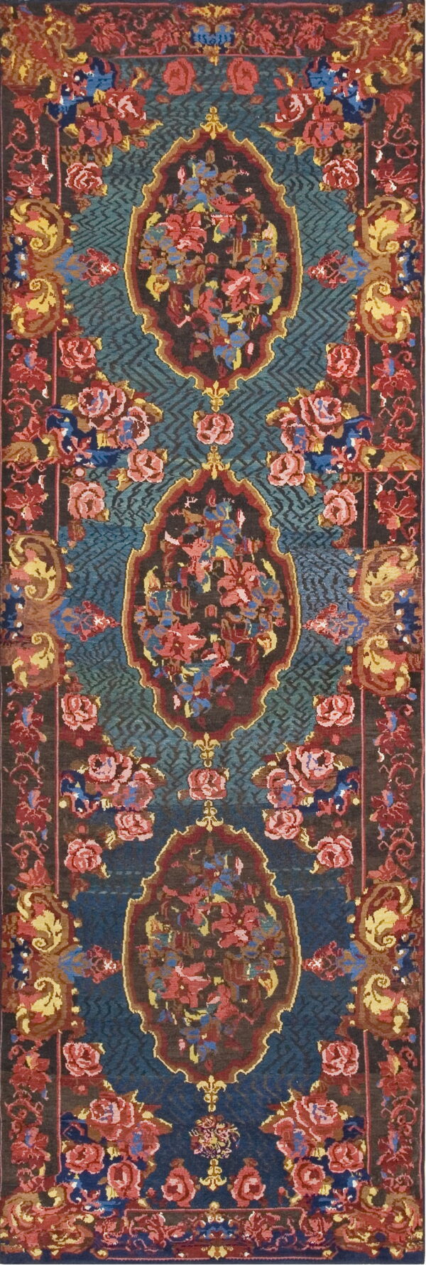 A runner rug with ornate red, pink, and yellow floral medallions on a teal geometric field.