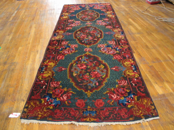 Runner rug featuring red, teal, gold, and blue floral medallions, lying on light wood flooring.