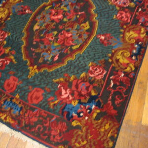 Traditional rug with red and gold floral motifs on a deep blue-green field over wood flooring.