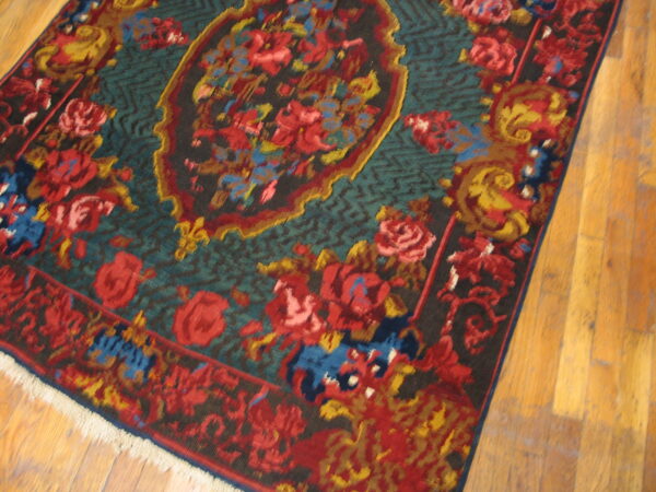 Traditional rug with red and gold floral motifs on a deep blue-green field over wood flooring.