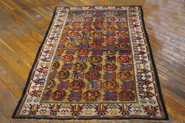 Small rug with a mustard field, block patterns in red and blue, and a detailed cream and black border on wood flooring.