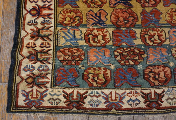 Geometric rug with rows of red and blue motifs on a teal and gold background, bordered in ivory.