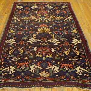 Dark blue rug with multi-colored geometric and stylized patterns displayed on honey-toned wood floors.