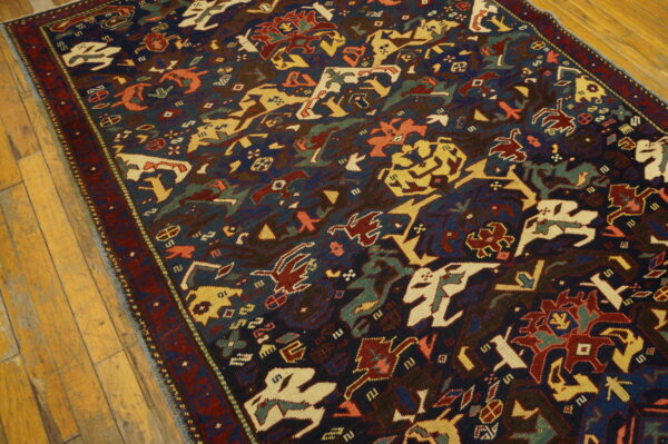 Short pile rug with stylized red, yellow, and cream figures on a dark blue field over light wood floors.