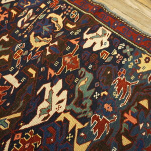 Intricate, multi-colored tribal pattern rug featuring red and cream on a dark blue field over distressed wood.