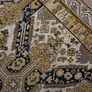 Detailed rug pattern in gold, navy, cream, and lavender rests diagonally on distressed wooden floorboards.