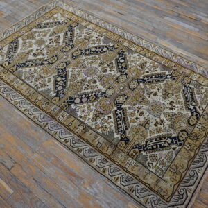 A cream and gold traditional rug featuring a dark blue central motif sits on aged wooden plank flooring.
