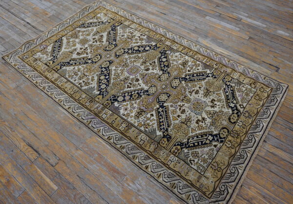 A cream and gold traditional rug featuring a dark blue central motif sits on aged wooden plank flooring.