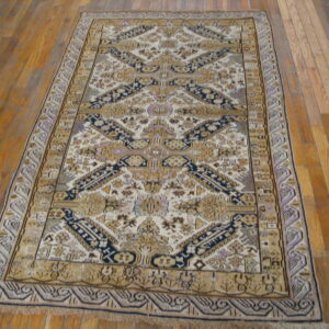 A rectangular rug featuring cream, gold, navy, and lavender geometric patterns is displayed on hardwood floorboards.