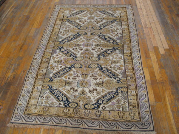 A rectangular rug featuring cream, gold, navy, and lavender geometric patterns is displayed on hardwood floorboards.