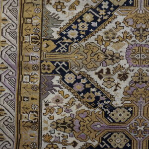 Intricate gold, navy, and lavender patterned rug border next to distressed wood flooring.